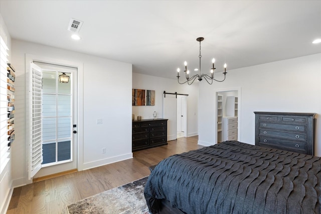 bedroom featuring dark hardwood / wood-style flooring, a spacious closet, a barn door, and an inviting chandelier