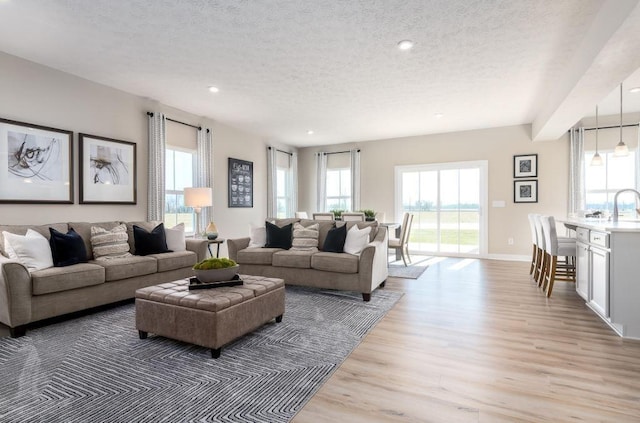 living room featuring sink, plenty of natural light, a textured ceiling, and light wood-type flooring