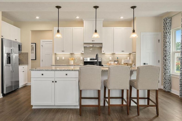 kitchen with stainless steel appliances, a kitchen island with sink, pendant lighting, and white cabinets