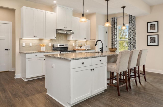 kitchen featuring stainless steel range with electric stovetop, light stone counters, a kitchen island with sink, and white cabinets