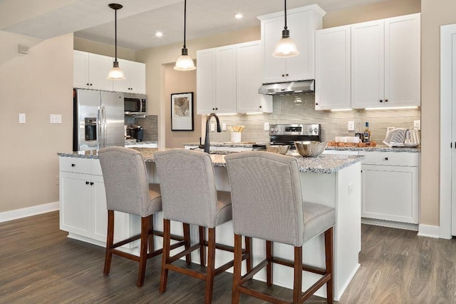 kitchen with appliances with stainless steel finishes, a center island with sink, white cabinets, and light stone counters