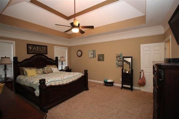 carpeted bedroom with a tray ceiling, ornamental molding, and ceiling fan