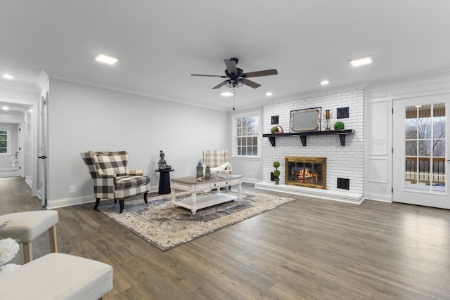 living room with dark wood-type flooring, ornamental molding, a brick fireplace, and a wealth of natural light