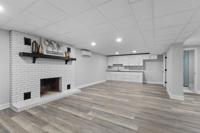 unfurnished living room with sink, a paneled ceiling, a wall mounted air conditioner, a brick fireplace, and light wood-type flooring