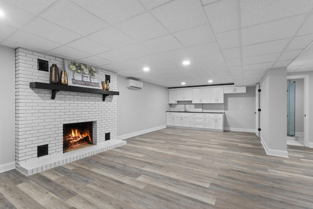 unfurnished living room with a paneled ceiling, a fireplace, sink, a wall unit AC, and light wood-type flooring