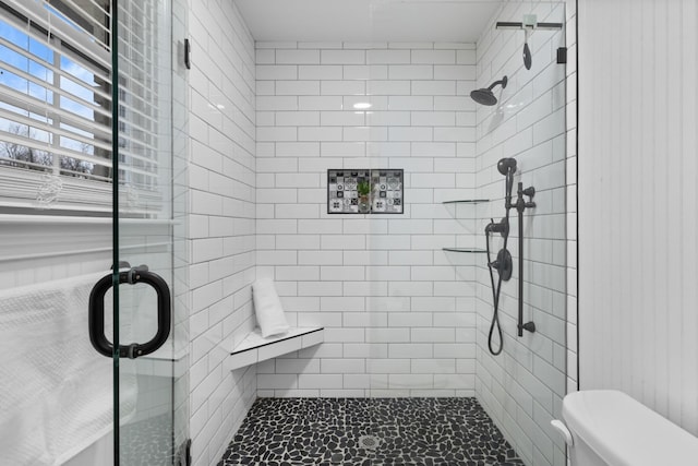 bathroom featuring a shower with door and toilet