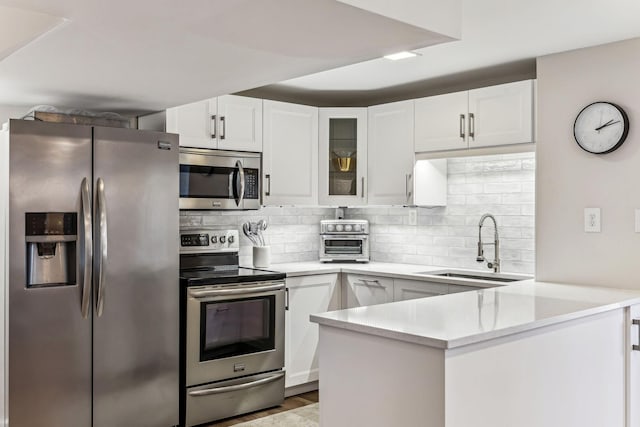 kitchen with backsplash, kitchen peninsula, white cabinets, and appliances with stainless steel finishes