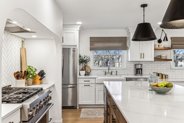 kitchen with pendant lighting, sink, appliances with stainless steel finishes, white cabinetry, and light stone countertops