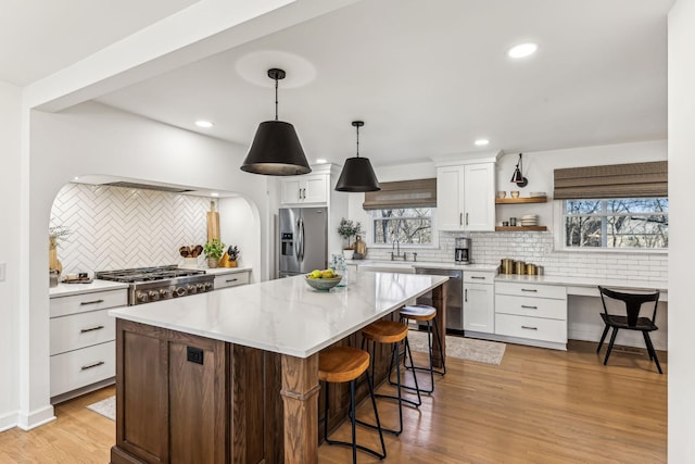 kitchen featuring appliances with stainless steel finishes, a center island, light hardwood / wood-style floors, white cabinets, and decorative light fixtures