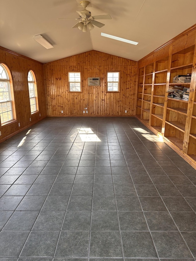 empty room featuring lofted ceiling with skylight, a wall mounted air conditioner, built in features, wooden walls, and ceiling fan