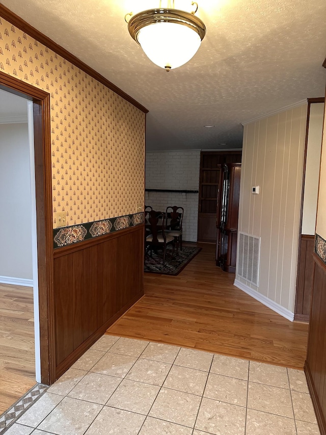 corridor featuring ornamental molding, light tile patterned floors, and a textured ceiling