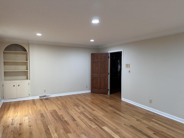 spare room with built in shelves, light hardwood / wood-style flooring, and ornamental molding