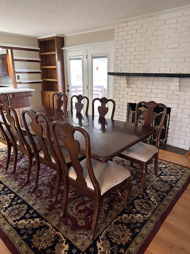 dining room featuring light hardwood / wood-style flooring, a textured ceiling, ornamental molding, brick wall, and a fireplace