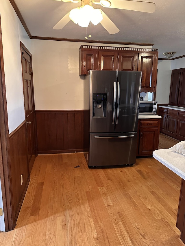 kitchen featuring ceiling fan, appliances with stainless steel finishes, ornamental molding, light hardwood / wood-style floors, and wood walls