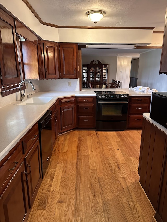 kitchen featuring sink, a textured ceiling, light hardwood / wood-style flooring, ornamental molding, and black appliances