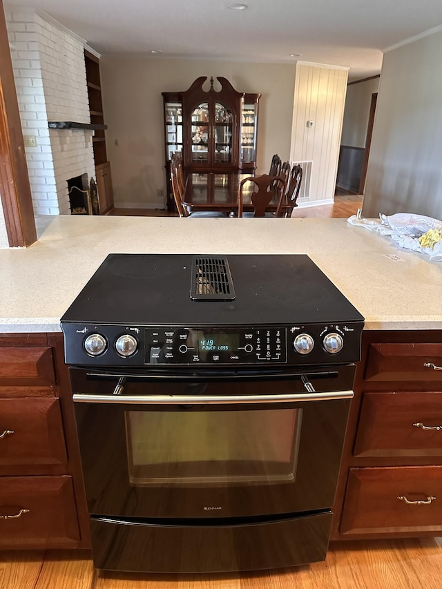 kitchen with black electric range oven, a brick fireplace, and light hardwood / wood-style flooring