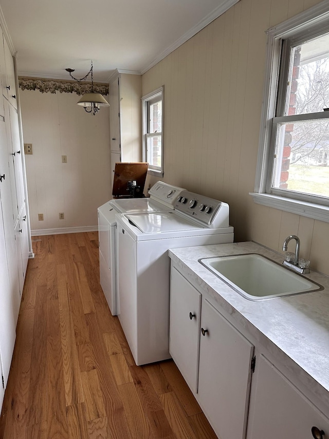 laundry room featuring sink, crown molding, washing machine and dryer, cabinets, and light wood-type flooring