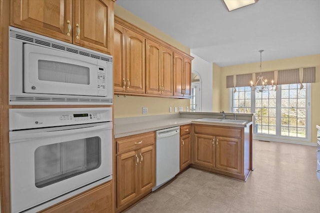 kitchen with decorative light fixtures, sink, white appliances, kitchen peninsula, and an inviting chandelier