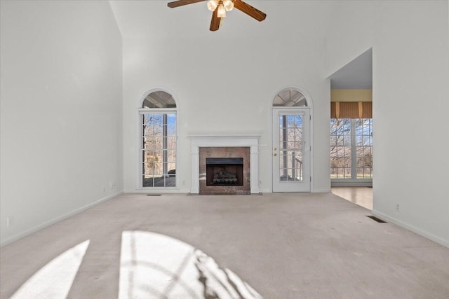 unfurnished living room with a towering ceiling, a healthy amount of sunlight, a fireplace, and light carpet