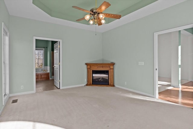 unfurnished living room featuring light carpet, a raised ceiling, and ceiling fan