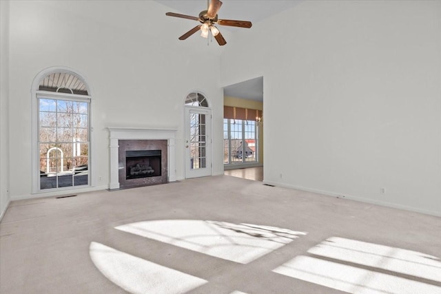 unfurnished living room featuring ceiling fan, a fireplace, light carpet, and a high ceiling