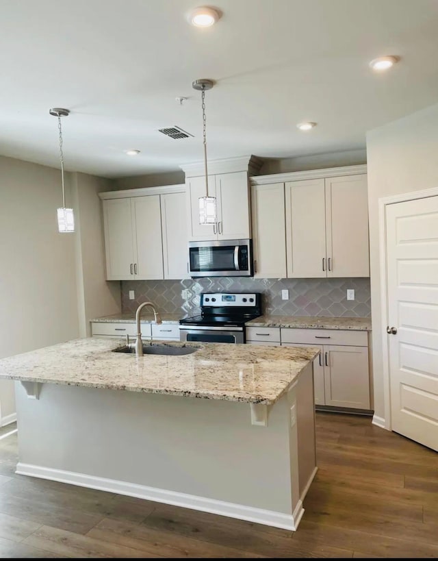 kitchen with appliances with stainless steel finishes, sink, pendant lighting, and a kitchen island with sink