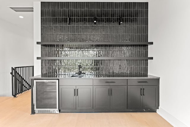 bar with wine cooler, sink, gray cabinetry, and light wood-type flooring