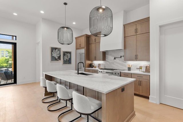 kitchen featuring tasteful backsplash, an island with sink, sink, premium appliances, and hanging light fixtures