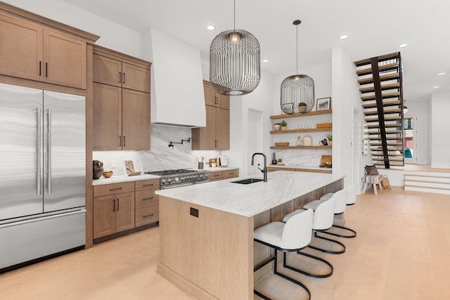 kitchen with sink, high end appliances, decorative light fixtures, custom range hood, and light stone countertops