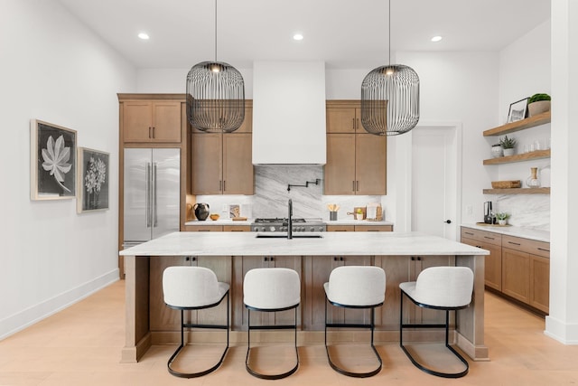 kitchen with a breakfast bar, a kitchen island with sink, stainless steel built in fridge, and wall chimney exhaust hood