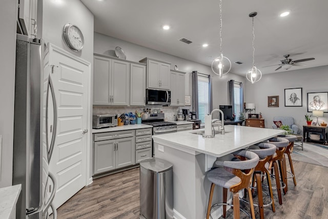 kitchen with gray cabinets, appliances with stainless steel finishes, pendant lighting, sink, and a kitchen island with sink