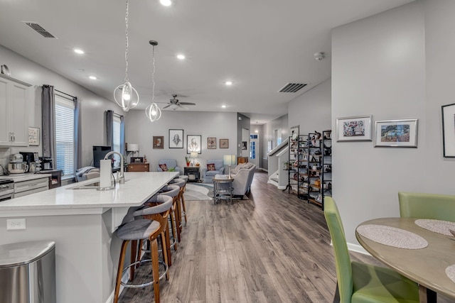 kitchen featuring sink, hardwood / wood-style flooring, white cabinetry, hanging light fixtures, and an island with sink