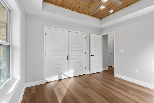 unfurnished bedroom featuring hardwood / wood-style floors, a tray ceiling, wooden ceiling, and a closet