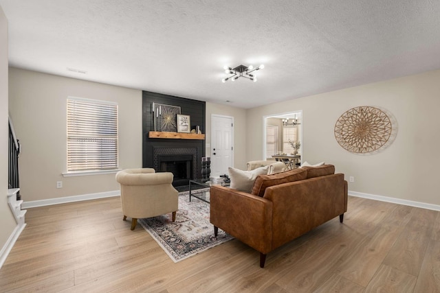 living room featuring a chandelier, light hardwood / wood-style floors, a brick fireplace, and a textured ceiling