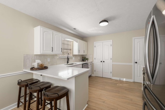 kitchen with sink, a breakfast bar, appliances with stainless steel finishes, white cabinets, and kitchen peninsula