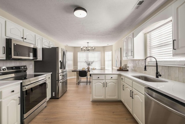 kitchen with white cabinetry, stainless steel appliances, kitchen peninsula, and sink