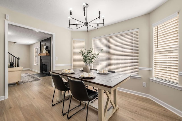 dining space featuring light hardwood / wood-style flooring, a notable chandelier, a fireplace, and a textured ceiling