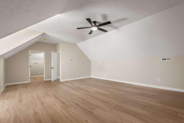 bonus room with ceiling fan, vaulted ceiling, a textured ceiling, and light wood-type flooring