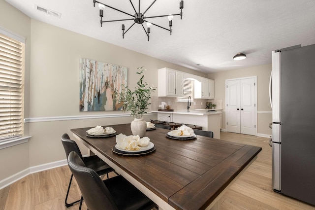 dining space featuring an inviting chandelier, sink, and light hardwood / wood-style flooring