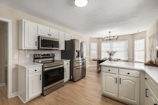 kitchen featuring appliances with stainless steel finishes, decorative light fixtures, white cabinets, decorative backsplash, and light hardwood / wood-style flooring