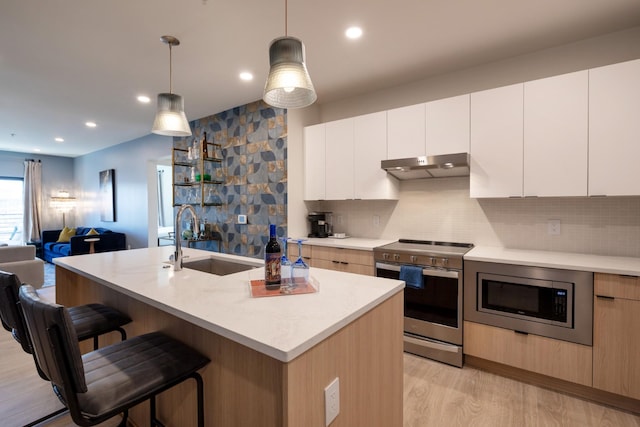 kitchen featuring sink, appliances with stainless steel finishes, white cabinets, a center island with sink, and decorative light fixtures