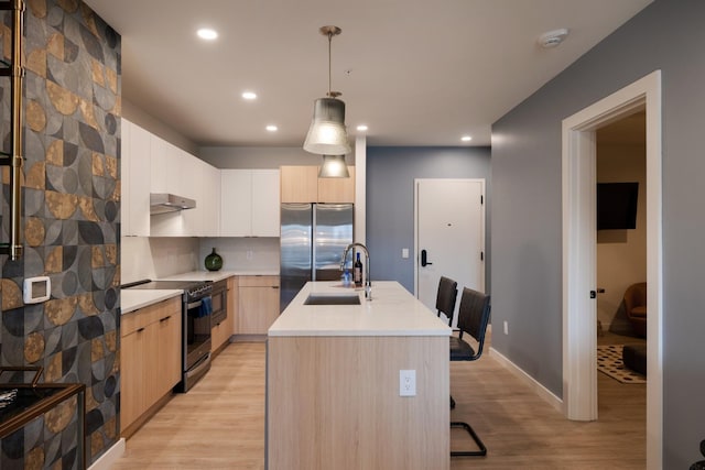 kitchen featuring sink, decorative light fixtures, light wood-type flooring, appliances with stainless steel finishes, and an island with sink