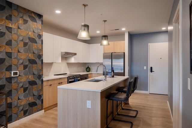 kitchen featuring sink, light hardwood / wood-style flooring, appliances with stainless steel finishes, a kitchen island with sink, and backsplash