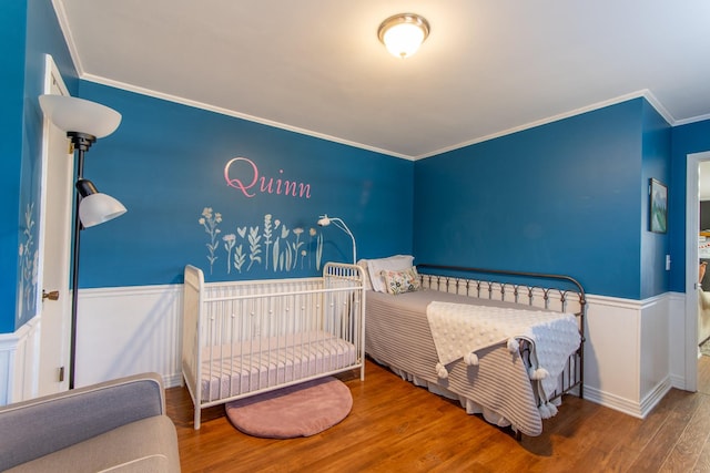 bedroom featuring crown molding, hardwood / wood-style floors, and a crib