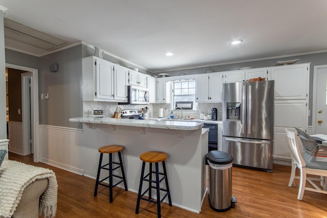 kitchen featuring white cabinetry, a kitchen breakfast bar, ornamental molding, light hardwood / wood-style floors, and stainless steel appliances