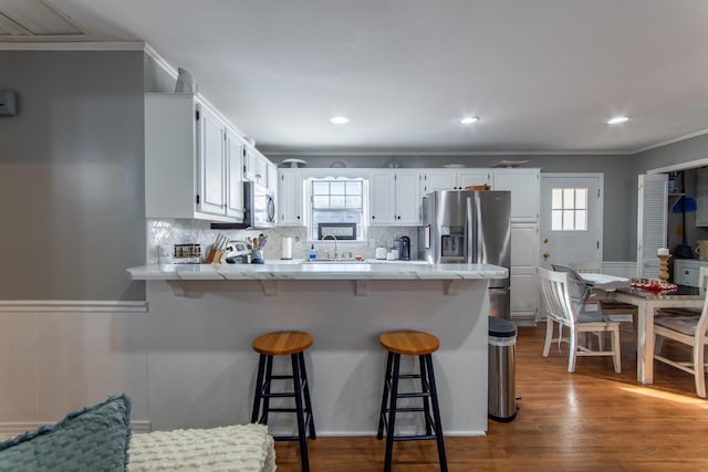 kitchen with appliances with stainless steel finishes, white cabinetry, a breakfast bar area, backsplash, and hardwood / wood-style flooring