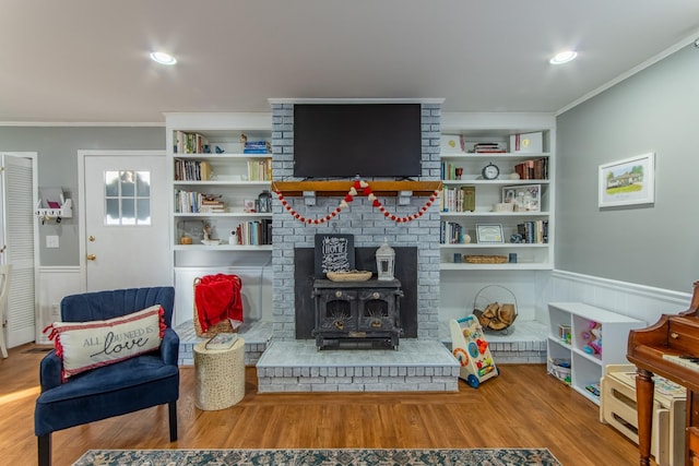 living room featuring crown molding, built in shelves, wood-type flooring, and a wood stove