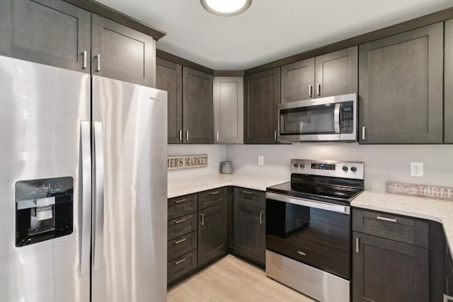 kitchen featuring stainless steel appliances, dark brown cabinets, light stone counters, and light hardwood / wood-style flooring