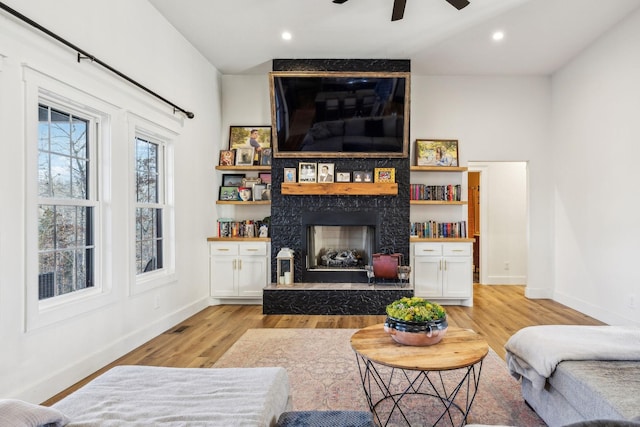 living room with ceiling fan, a large fireplace, and light wood-type flooring