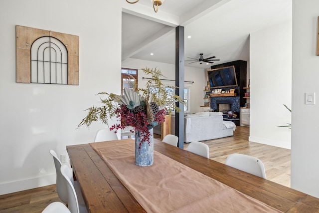 dining room with beamed ceiling, ceiling fan, a fireplace, and light hardwood / wood-style floors